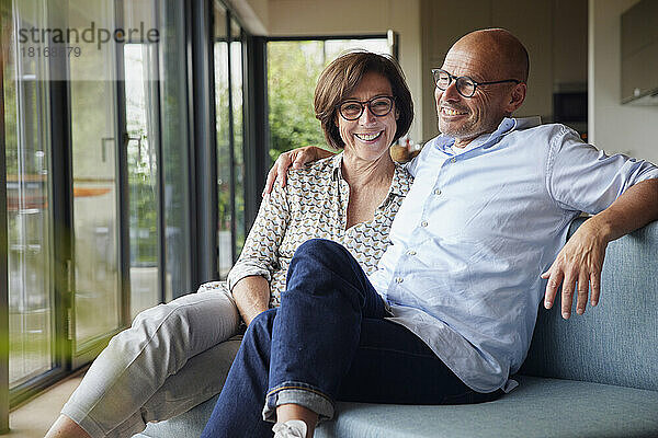 Fröhliches Seniorenpaar sitzt zu Hause gemeinsam auf dem Sofa
