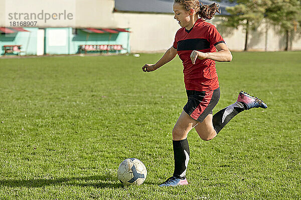 Mädchen kickt an einem sonnigen Tag Fußball auf dem Feld