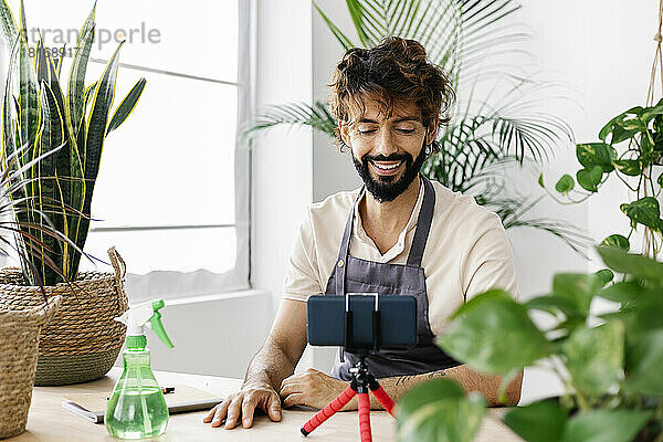 Glücklicher Mann mit Mobiltelefon auf Stativ im Pflanzenladen