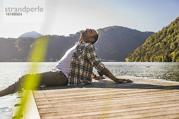 Reifer Mann entspannt sich mit geschlossenen Augen auf dem Steg über dem See
