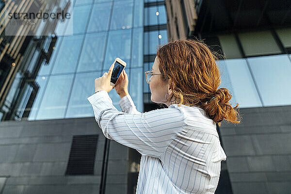 Junge Geschäftsfrau fotografiert Gebäude per Handy