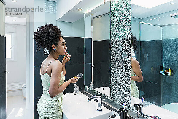 Frau mit lockigem Haar schminkt sich im heimischen Badezimmer das Gesicht