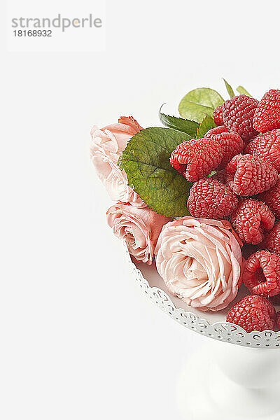 Pink roses with juicy raspberries on pedestal cakestand against white background