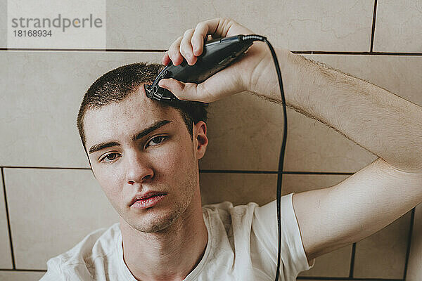 Einsamer junger Mann rasiert Haare mit Elektrorasierer im Badezimmer