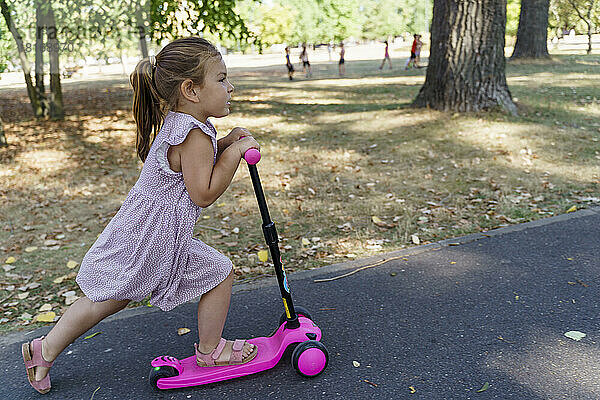 Mädchen fährt Tretroller auf Fußweg im Park