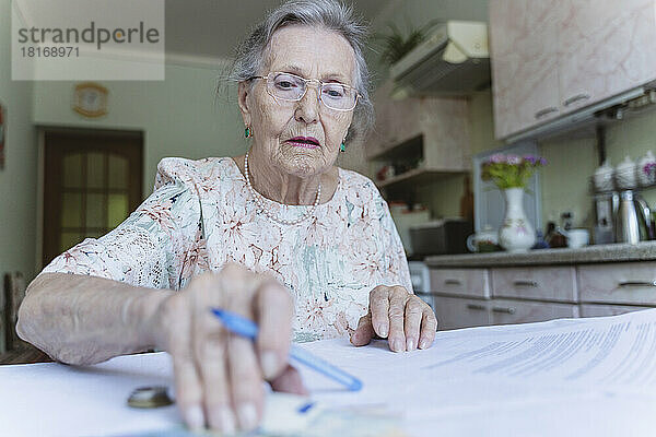 Ältere Frau  die zu Hause Geld zählt und Papierkram erledigt