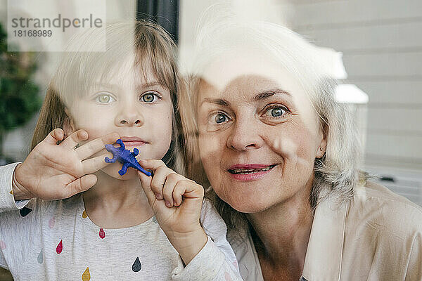 Nachdenkliche Großmutter und Enkelin mit Spielzeug  die aus dem Fenster schauen