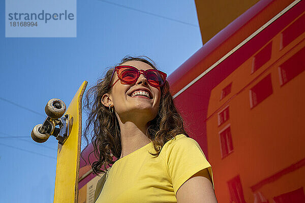Glückliche Frau mit Sonnenbrille und gelbem Skateboard