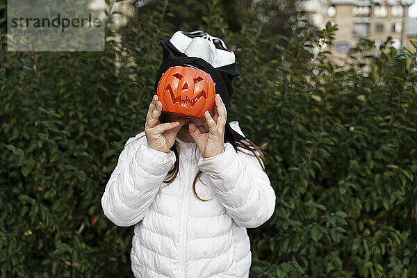 Mädchen bedeckt Gesicht mit Kürbiskorb an Halloween