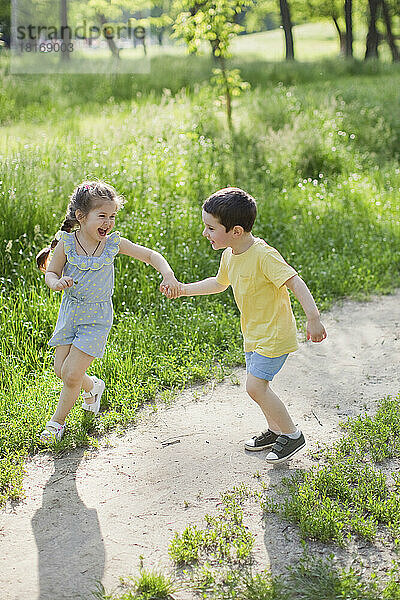 Fröhliches süßes Mädchen  das mit seinem Bruder im Park spielt