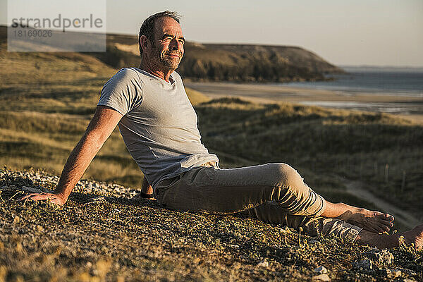 Mature man relaxing on hill at sunset