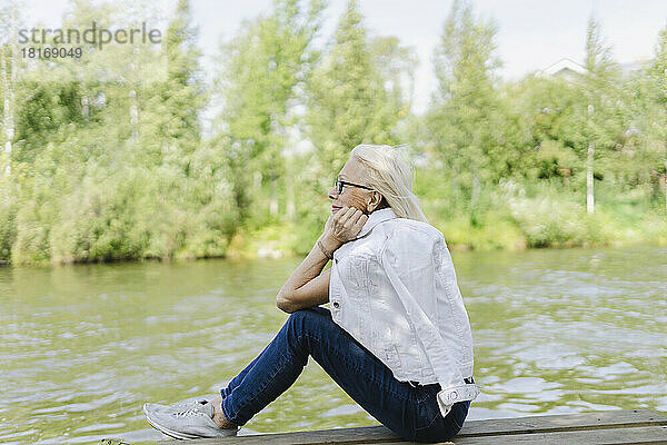 Ältere Frau träumt davon  auf einem Steg in der Nähe des Sees zu sitzen