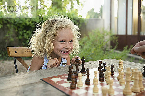 Fröhliches blondes Mädchen mit Schachbrett auf dem Tisch im Garten