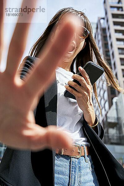 Frau mit Smartphone zeigt Stopp-Geste mit der Hand