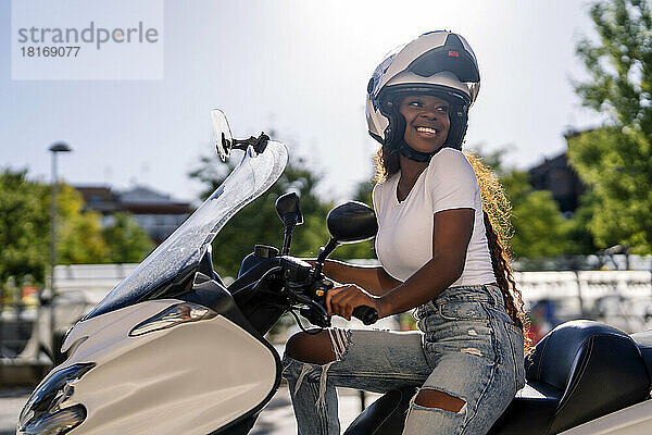 Happy young woman wearing helmet on scooter