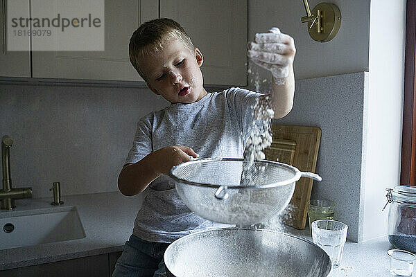 Netter Junge sieben Mehl für die Kuchenzubereitung zu Hause