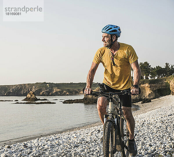 Mann mit Fahrradhelm fährt Fahrrad am Strand