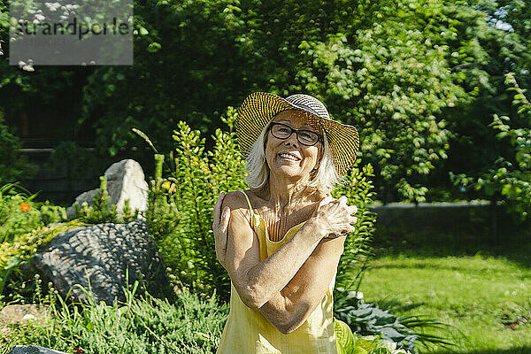 Glückliche ältere Frau umarmt sich an einem sonnigen Tag im Garten