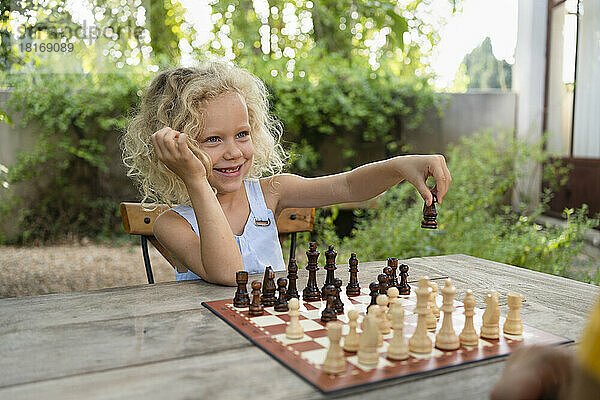Lächelndes Mädchen  das Schach im Garten spielt
