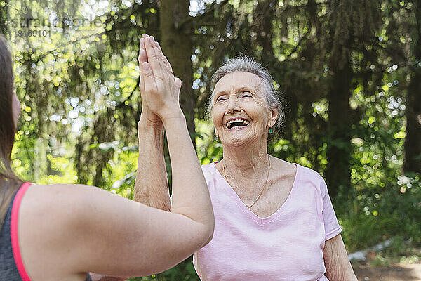 Fröhliche ältere Frau berührt die Hand eines Fitnesstrainers im Park