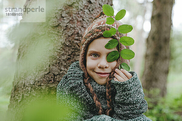 Lächelnd hält er Blätter am Baum im Wald