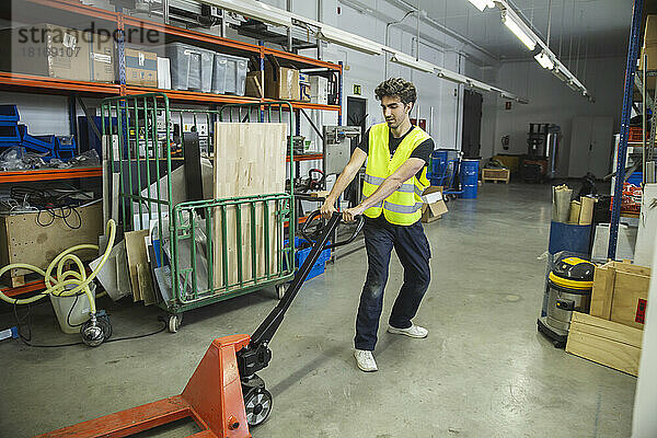 Blue-collar worker pulling hand truck in warehouse
