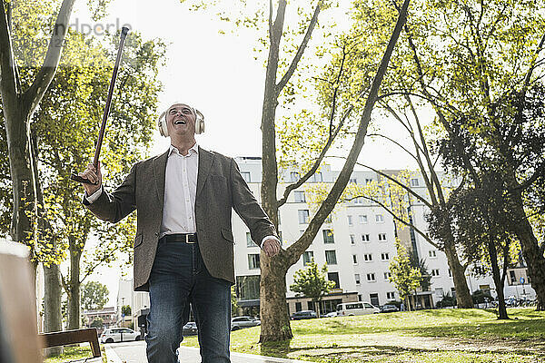 Glücklicher älterer Mann mit Gehstock  der über drahtlose Kopfhörer Musik hört und auf dem Fußweg tanzt