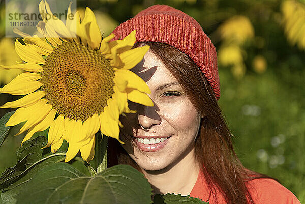Lächelnde Frau mit Strickmütze und Sonnenblume an einem sonnigen Tag