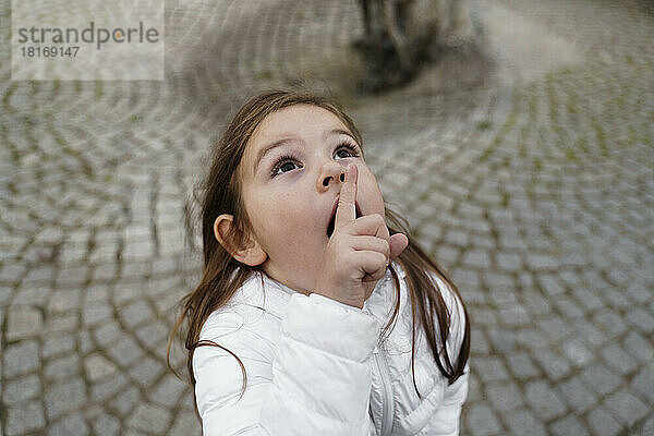 Nettes Mädchen mit dem Finger auf den Lippen  das nach oben schaut