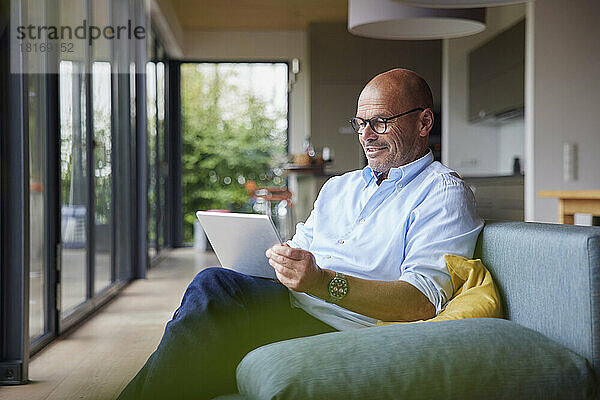 Lächelnder Mann mit Tablet-PC  der zu Hause auf dem Sofa sitzt