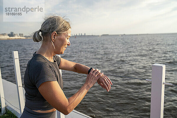 Lächelnde Frau überprüft die Zeit mit einer Smartwatch vor dem Meer