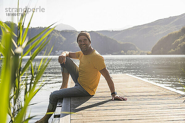Glücklicher reifer Mann  der im Urlaub auf einem Steg über dem See sitzt