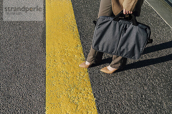 Businesswoman with laptop bag standing by yellow line on road