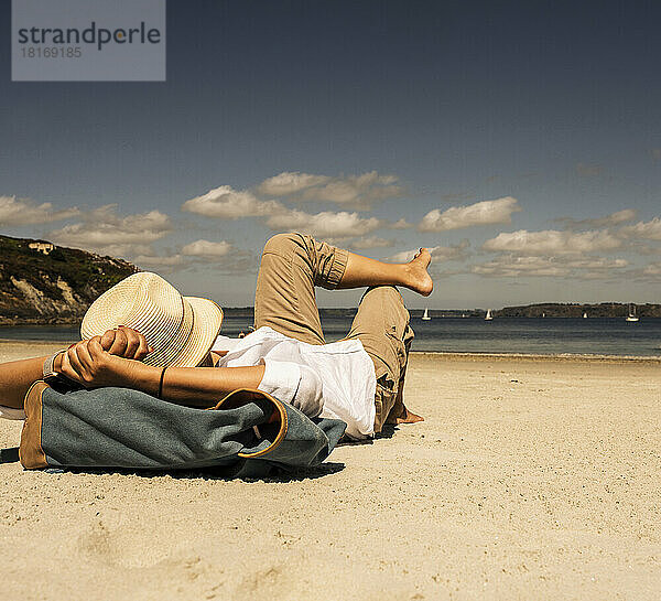 Reife Frau mit Hut entspannt sich an einem sonnigen Tag am Strand