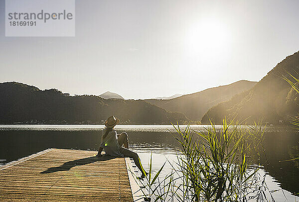 Frau mit Hut sitzt auf Steg über See bei Bergen