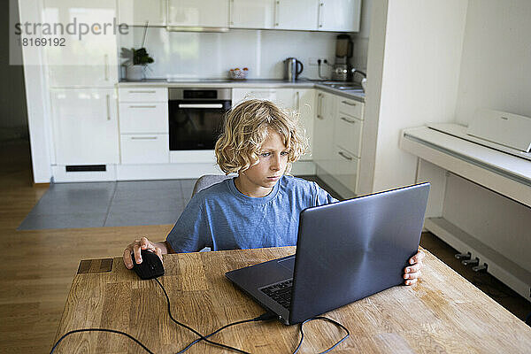 Junge lernt zu Hause mit Laptop am Tisch