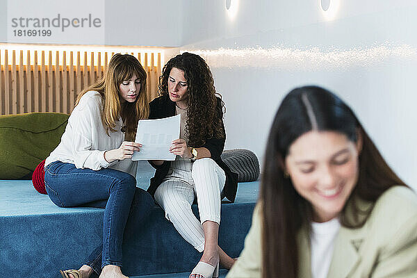 Zwei Geschäftsfrauen lesen ein Dokument in der Bürolounge  im Vordergrund ein Kollege