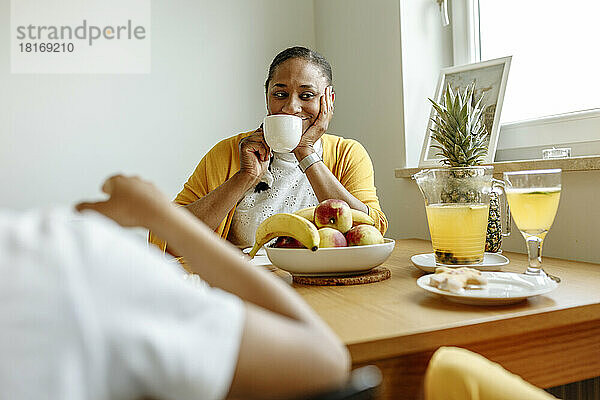 Lächelnde Frau trinkt Kaffee am Esstisch