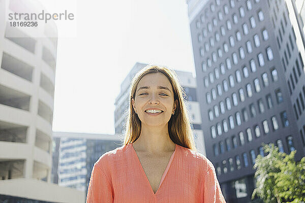 Lächelnde schöne Frau vor dem Gebäude an einem sonnigen Tag