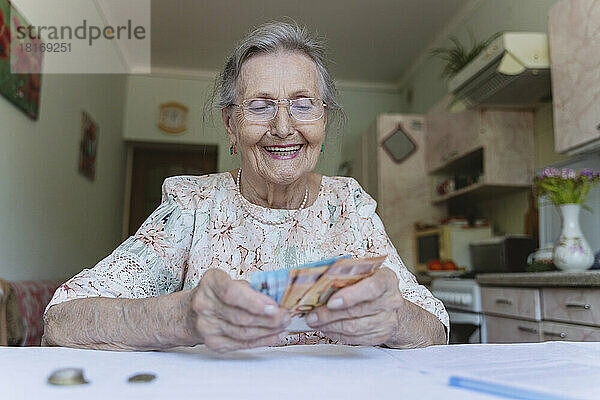 Glückliche ältere Frau  die zu Hause Banknoten zählt