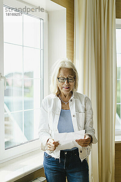 Ältere Frau liest zu Hause am Fenster