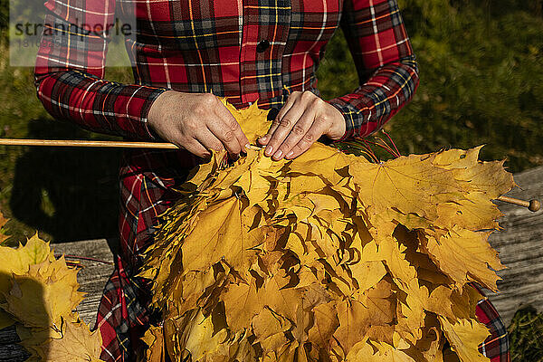 Hände einer Frau  die einen Schal aus Herbstblättern strickt