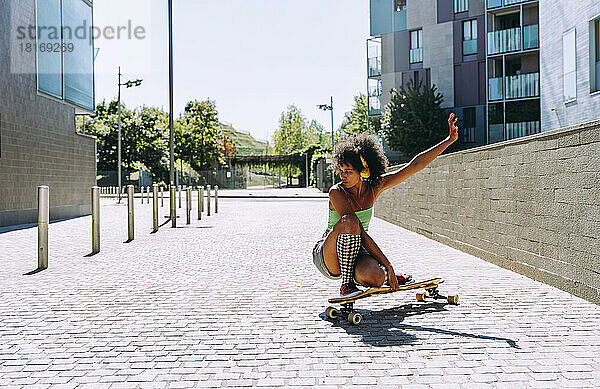 Frau kauert auf Skateboard vor Gebäude