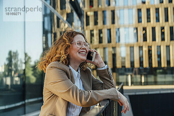 Glückliche Geschäftsfrau  die vor dem Bürogebäude mit dem Mobiltelefon spricht