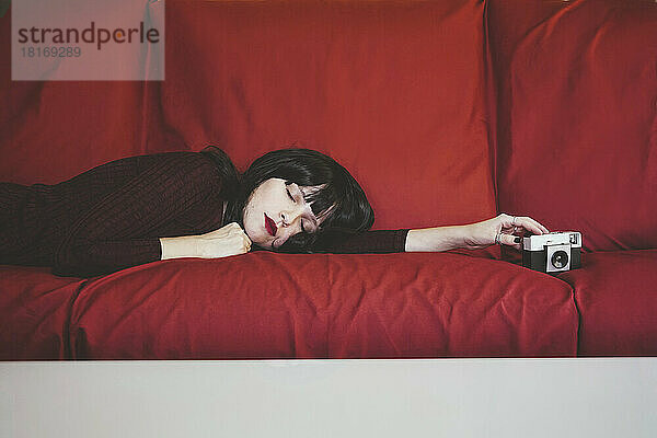 Frau mit analoger Kamera entspannt auf roter Couch