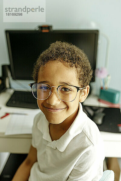Lächelnder Junge mit Brille vor dem Desktop-PC zu Hause