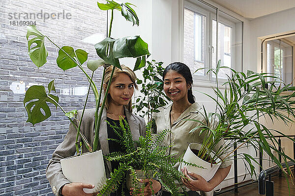 Young businesswomen carrying potted plants in modern office