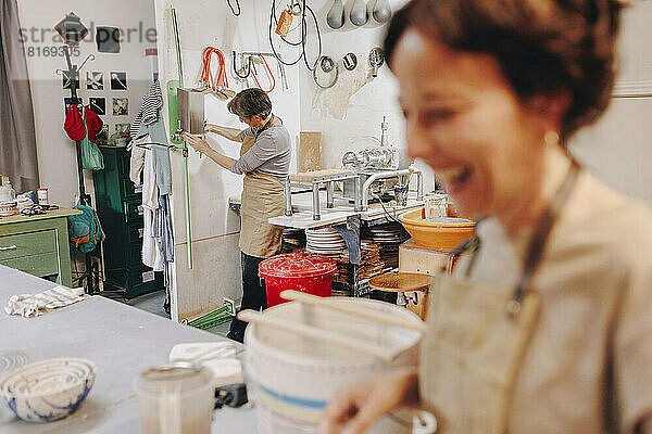 Glücklicher Unternehmer mit Kollegen  der im Hintergrund in der Keramikwerkstatt arbeitet