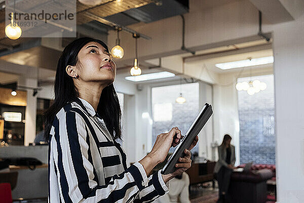 Junge Geschäftsfrau steht im Coworking-Büro und nutzt digitales Tablet