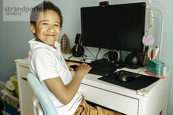 Lächelnder Junge vor dem Desktop-PC zu Hause